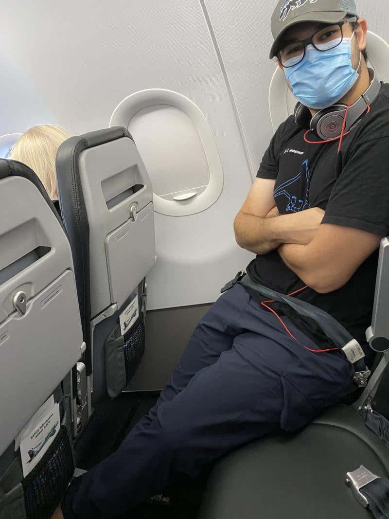 Picture of middle seat blocked on flight and male passenger with face mask on for safety.