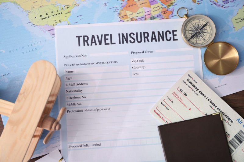 Photo of travel insurance application, world map and travel documents.