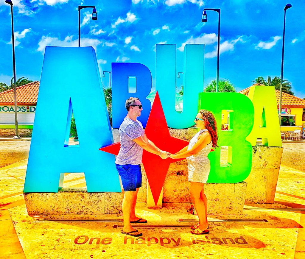 Boy and Girl holding hands in front of giant ARUBA sign