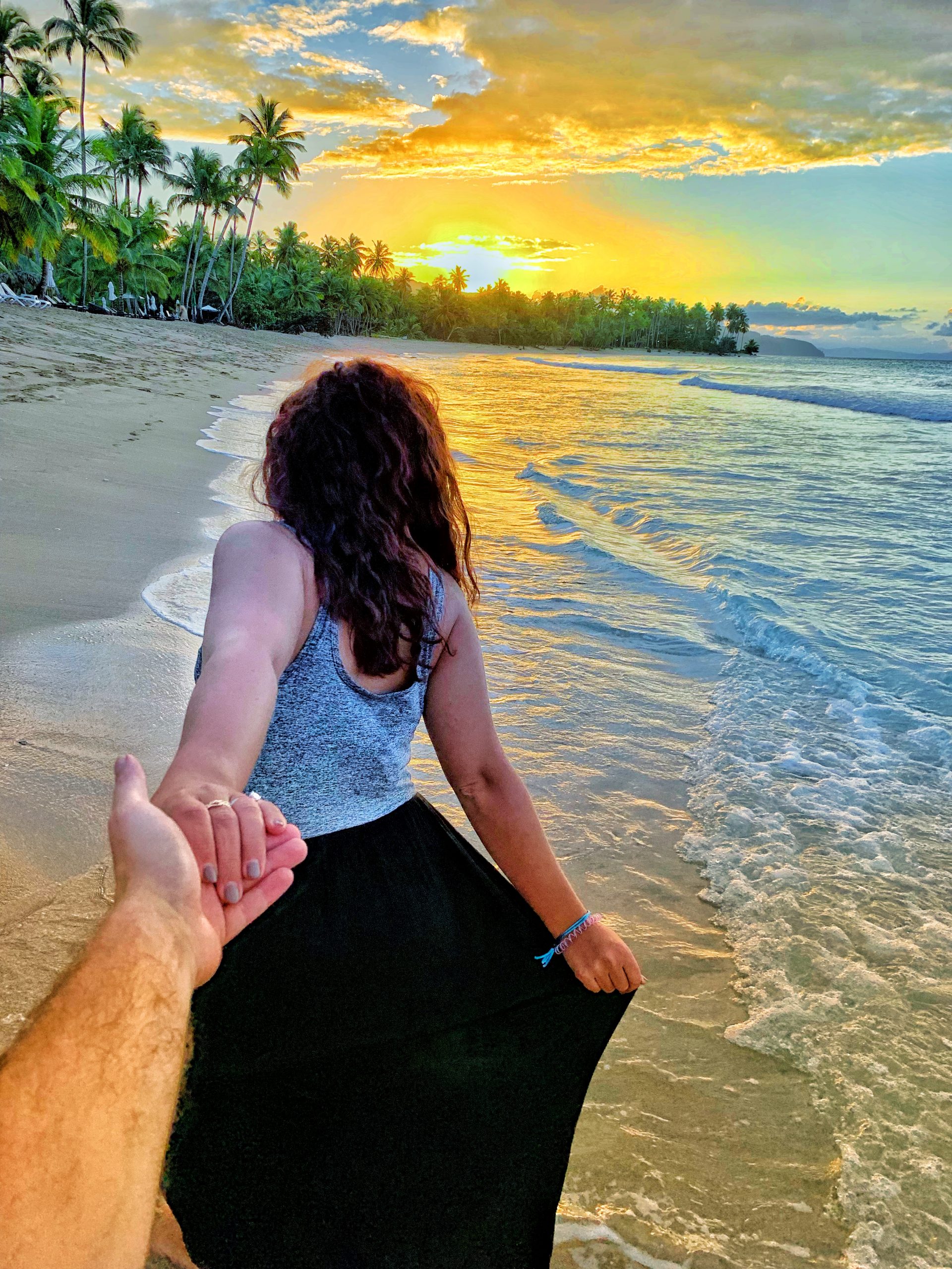 Boy holding girls hand walking along beach