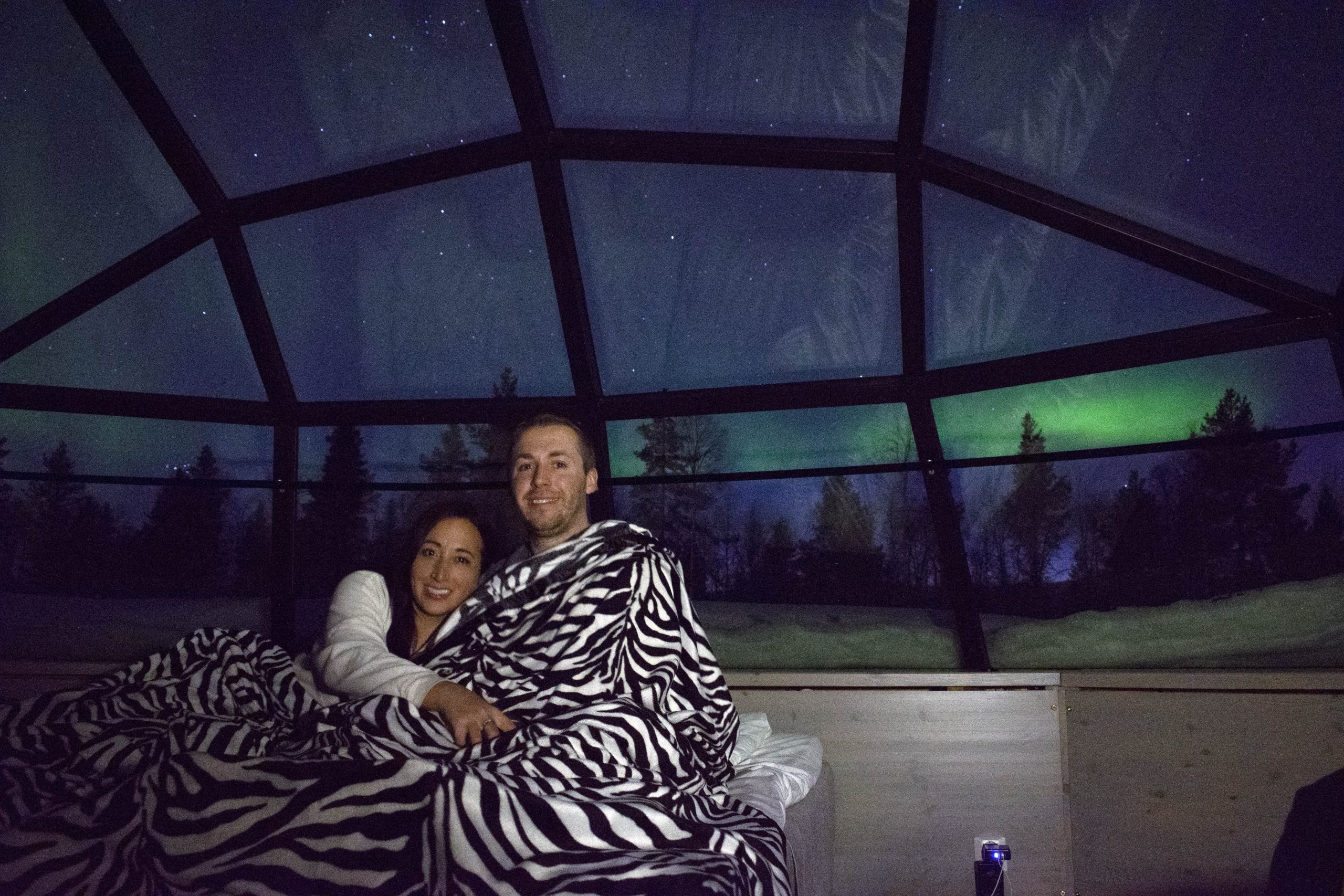 Couple sitting in Glass Igloo with Northern lights in background