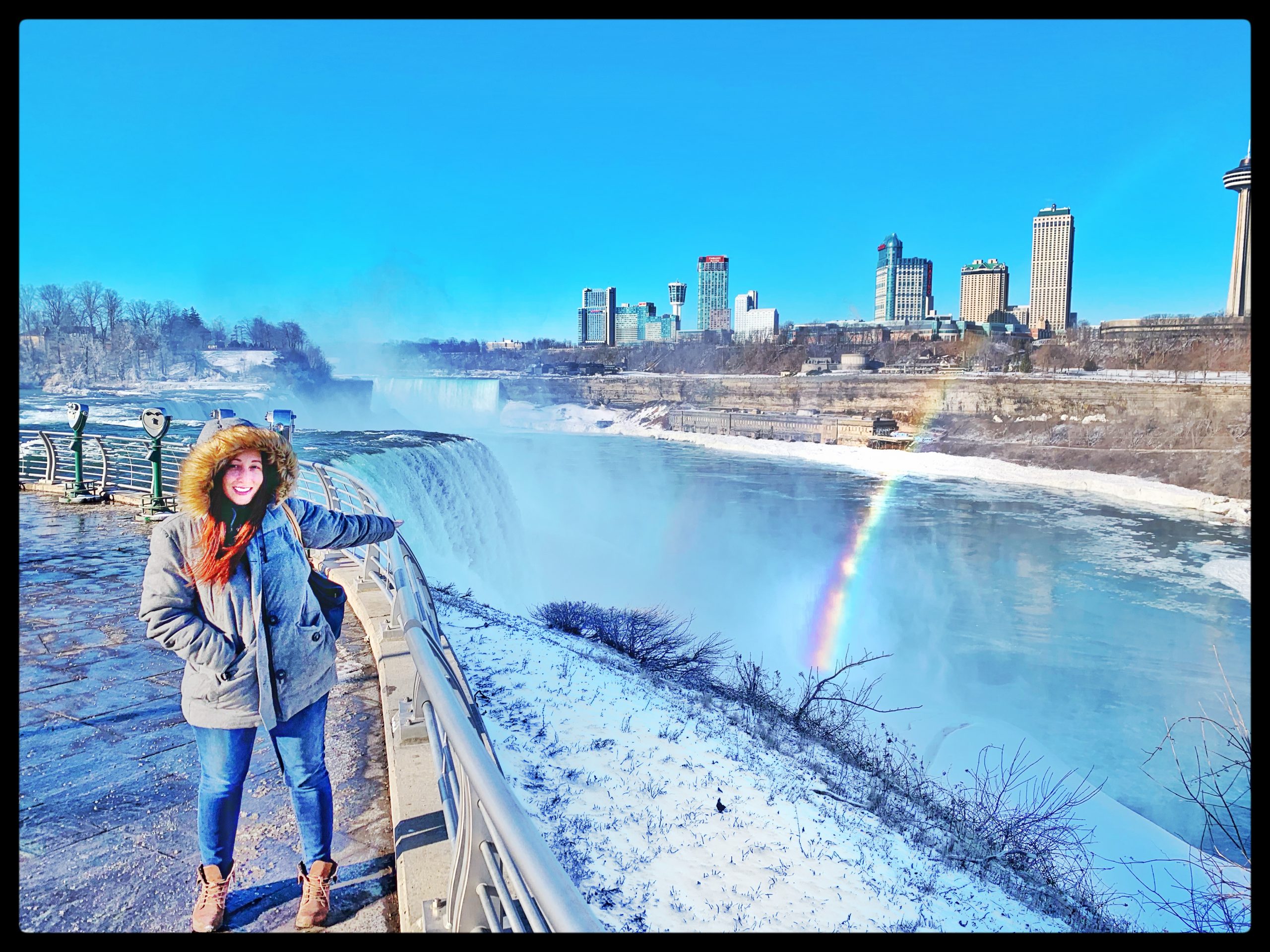 Girl standing next to Niagara Falls and a rainbow in the background