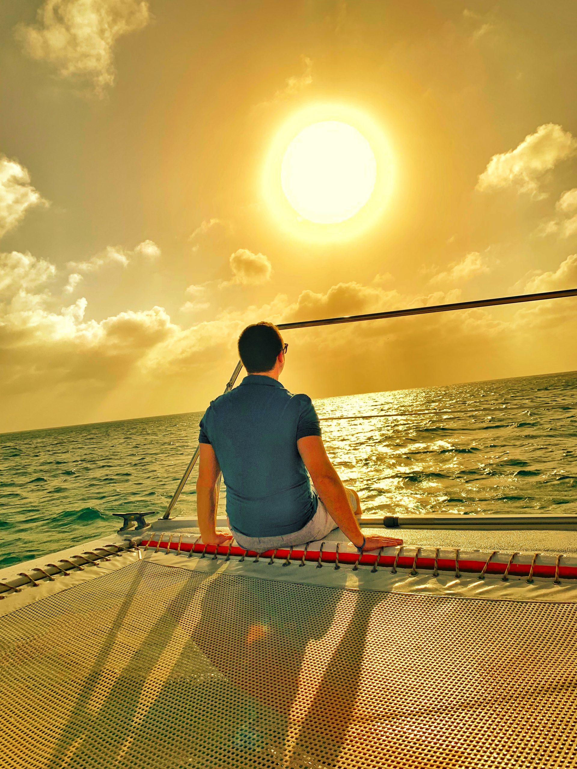 Man sitting on the edge of a boat staring into the sun and ocean