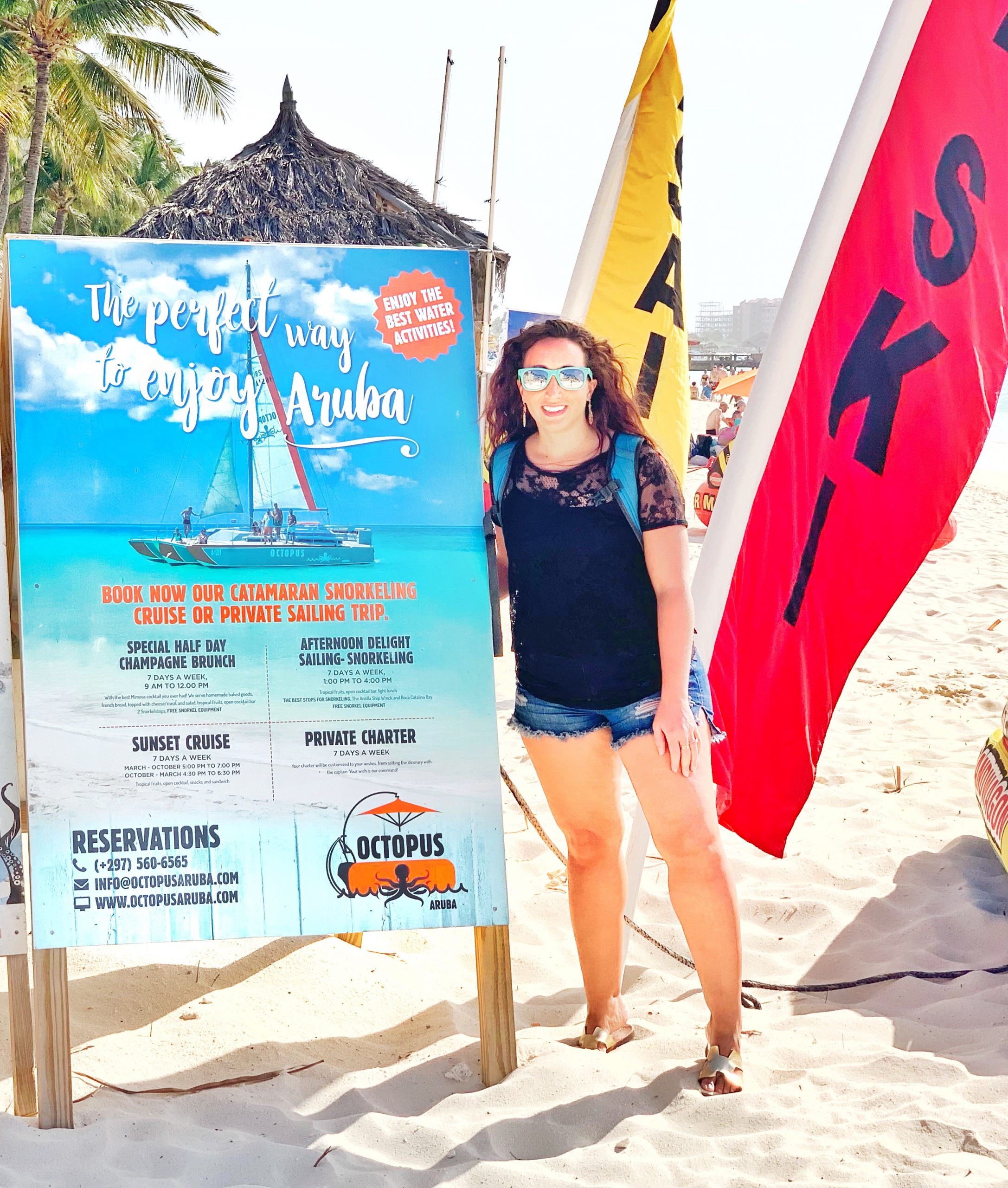 Girl standing next to Octopus Aruba Sailing sign on beach